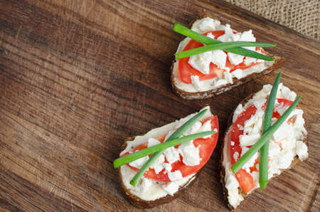slices of rye bread with sire feta, tomato and onion on a wooden board.  Selective focus.の写真素材