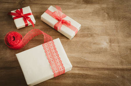 Vintage kraft boxes with gifts, tied with red ribbons on rustic wooden background. View from above with copy space.の写真素材