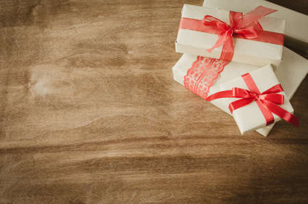 Vintage kraft boxes with gifts, tied with red ribbons on rustic wooden background. View from above with copy space.の写真素材