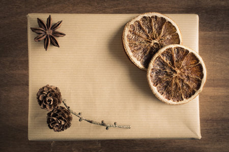 Vintage Christmas Kraft Gift Box in Rustic Style Decorated with Cones, Star Anise and Dried Orange Slices on Wooden Background. View from above with copy space.の写真素材