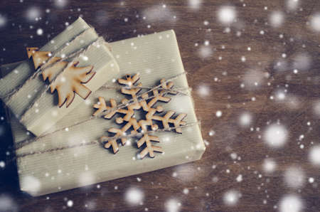 Kraft Boxes with Gifts Decorated with Wooden Snowflake, Christmas Tree and Jute on Wooden Background. Vintage Image with Drawn Snowfall. Christmas in Rustic Style. View from above with copy space.の写真素材