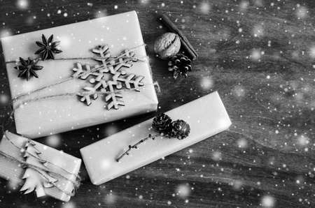Kraft Boxes with Gifts Decorated with Wooden Snowflake, Christmas Tree and Jute on Wooden Background. Vintage Image with Drawn Snowfall. Christmas in Rustic Style. View from above with copy space.の写真素材