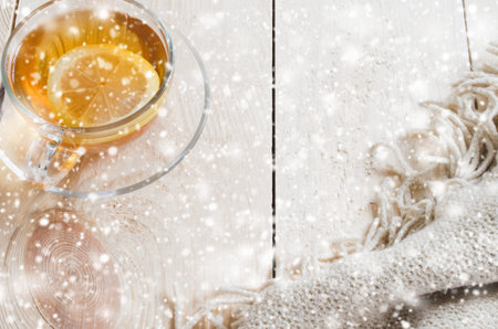 Cozy and soft winter background. Cup of tea with lemon and warm knitted blanket on a vintage wooden board. Holidays at home. Selective Focus. Snow Falling Effect.の写真素材