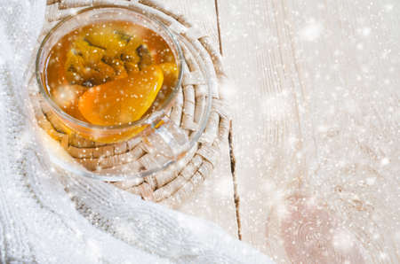 Cozy and soft winter background. Cup of tea with lemon and warm knitted sweater or blanket on a vintage wooden board. Holidays at home. Snow Falling Effect. Selective Focus.の写真素材