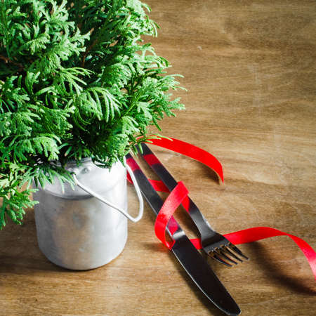 Rustic Table Setting for Christmas. Fir Branches in Vintage Can and Cutlery Decorated with Red Ribbon on Wooden Background. Selective Focus. Space for Text.の写真素材