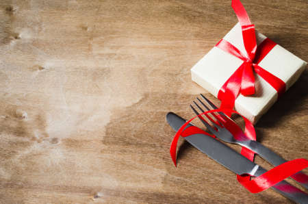 Present and Cutlery Decorated with Red Ribbon on Wooden Background. Selective Focus. Space for Text.の写真素材