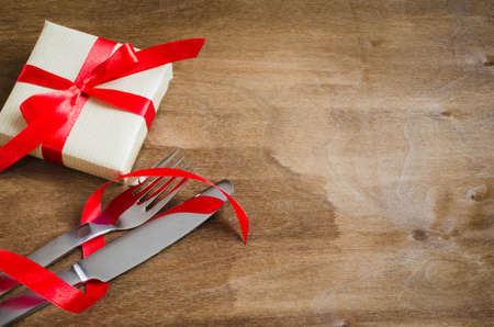 Present and Silverware Decorated with Red Ribbon on Wooden Background. Selective Focus. Space for Text.の写真素材
