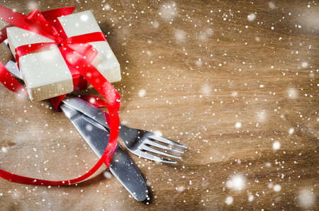 Gift Box and Cutlery Decorated with Red Ribbon on Wooden Background. Selective Focus. Space for Text. Toned image. Snow effect.の写真素材
