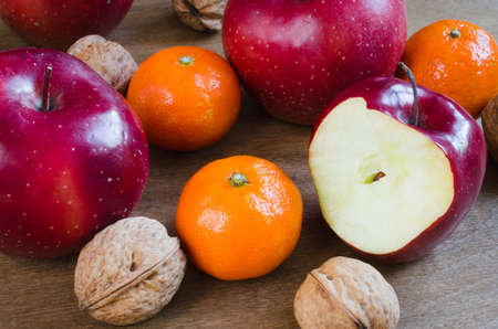 Organic whole and bitten off apples, tangerines and walnuts on a wooden background. Selective Focus. Rustic style.の写真素材