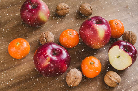 Organic apples, tangerines and walnuts on a wooden background. Selective Focus. Rustic style. Toned image. Snow effect.の写真素材