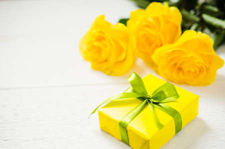 Mother's day, Valentine's or birthday concept. Present and yellow roses on white wooden background. Copy space. Selective focus.の写真素材