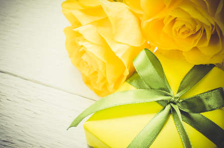 Mother's day, Valentine's or birthday concept. Present and yellow roses on white wooden background. Vintage Style. Toned Image. Copy space. Selective focus.の写真素材