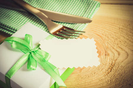 Dining Table Setting. Cutlery with Empty Tag and Present on Linen Napkin on Rustic Wooden Background. Copy Space. Selective Focus.の写真素材