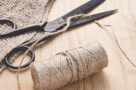 Old scissors, skein jute twine and burlap on a wooden background. Rustic style. Selective focus.の写真素材