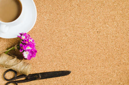 Flowers, scissors and jute next to cup of coffee on cork board.の写真素材