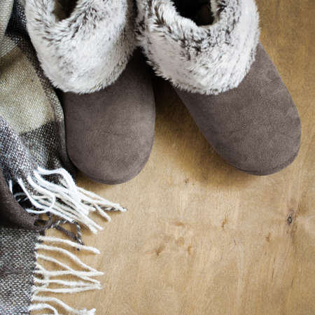 Warm home clothes. Woolen plaid and home slippers on wooden background.の写真素材