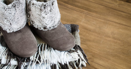 Warm home clothes. Woolen plaid and home slippers on wooden background.