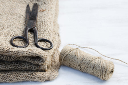 Old scissors, skein jute twine and burlap on a wooden background. Rustic style. Selective focus.