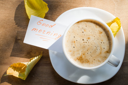Cappuccino or coffee latte with foam in white cup and the Inscription Good Morning on wooden table....