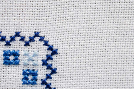 Embroidered fragment on white flax by white and blue cotton threads. Embroidery texture for background. Cross stitch. Ukrainian ethnic ornament.の写真素材