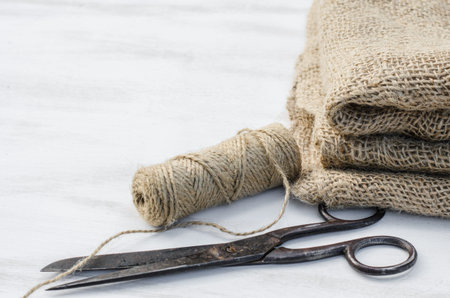 Old scissors, skein jute twine and burlap on a wooden background. Rustic style. Selective focus.