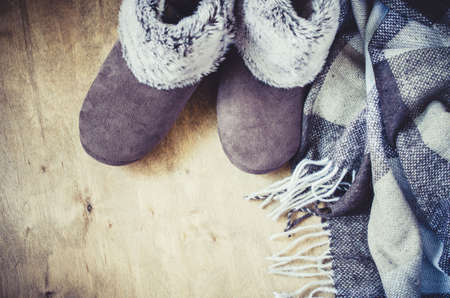 Warm home clothes. Woolen plaid and home slippers on wooden background.の写真素材