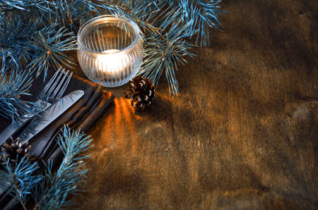 Vintage or rustic Christmas table setting with candle and wooden decorations. Cutlery on linen napkin on rustic wooden background - country style. Selective focus, space for text.の写真素材