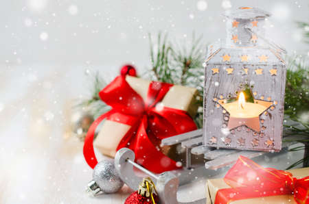 Christmas lantern with candle and gift with xmas decorations over white wooden background. Magic lightning background, copy space. Snow effect.の写真素材