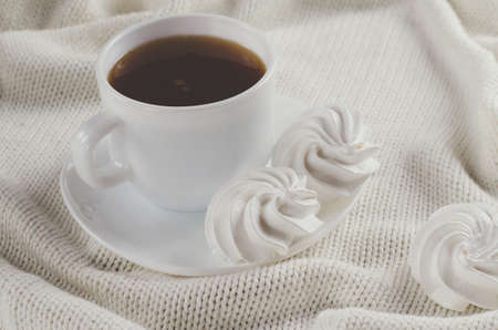 Fresh delicious white meringue cookies and cup of hot tea on knitted plaid. Cozy atmosphere.の写真素材