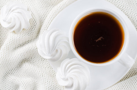 Fresh delicious white meringue cookies and cup of hot tea on knitted plaid. Cozy atmosphere. Top...
