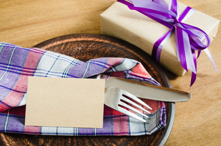 Dining Table Setting. Cutlery with Empty Tag and Present on Linen Napkin on Rustic Wooden Background. Father's Day Concept. Copy Space. Selective Focus.の写真素材