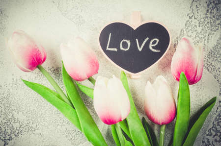 Holiday postcard. Bouquet of pink tulips and little blackboard with inscription love on white background. Greeting card for Valentine's Day or birthday. Top view, copy space.の写真素材