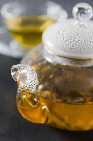 Cup of delicious herbal tea and glass teapot on dark background.の写真素材