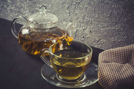 Cup of delicious herbal tea and glass teapot on dark background. Copy spaceの写真素材