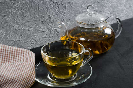 Cup of delicious herbal tea and glass teapot on dark background. Copy spaceの写真素材