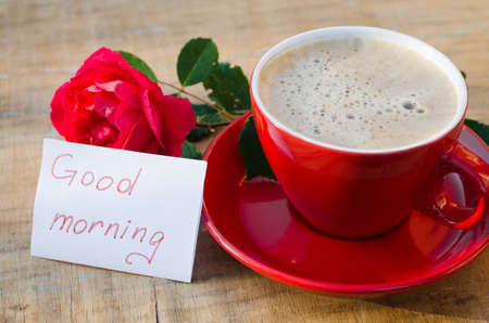 Coffee cup with red rose flower and notes good morning on wooden rustic table from above, breakfast on Mothers day, Womens day or Valentines dayの写真素材