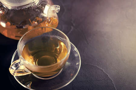 Cup of delicious herbal tea and glass teapot on dark background. Top view with copy spaceの写真素材