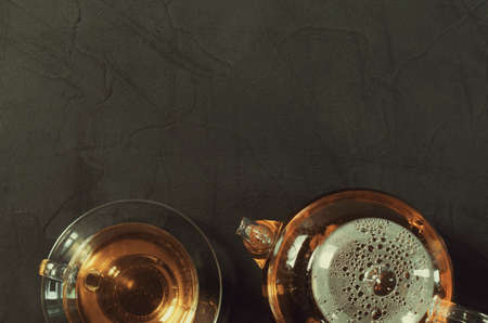 Cup of delicious herbal tea and glass teapot on dark background. Top view with copy spaceの写真素材