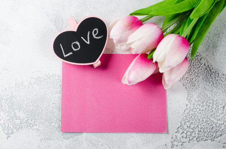 Empty holiday postcard. Bouquet of pink tulips and little blackboard with inscription love on white background. Greeting card for Valentine's Day or birthday. Top view, copy space.の写真素材