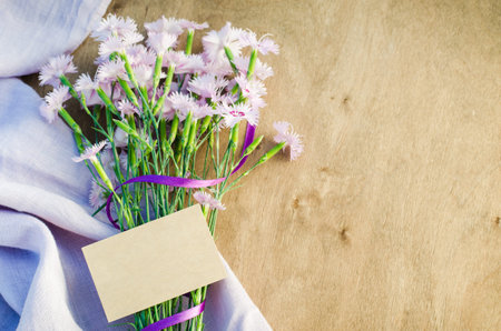 Delicate flowers and empty greeting card on a wooden background.