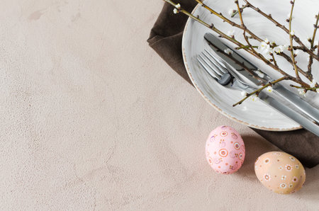 Easter table setting in beige color with spring flowering branches and cutlery.