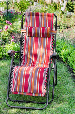 Empty chaise-longue in the blooming summer sunny garden on the grass. Cozy patio for rest.の写真素材