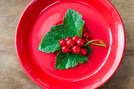 Fresh ripe organic red currant in plate on wooden background. Selective focus, rustic style.
