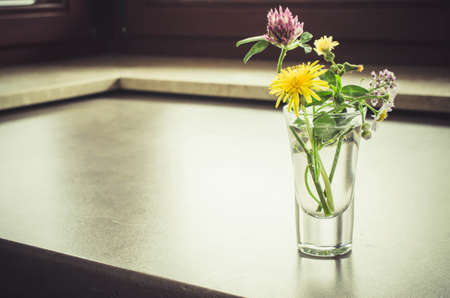 A small bouquet of wildflowers in a glass. Vintage toned image.の写真素材