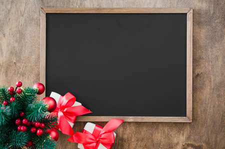 Empty blackboard with christmas decoration, red gift box, fir branches. Chalk board and Christmas trinkets. Xmas background with copy space for inscription, top view.の写真素材