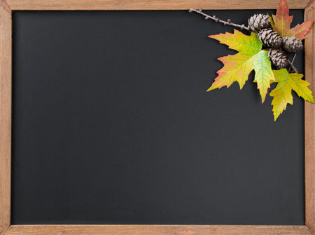 Autumn background with fall leavesand and cones on wooden table. Black chalkboard in center with...