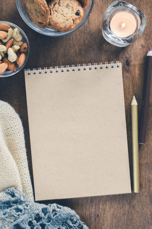 Flat lay of blank brown notebook with knitted blanket and snacks on wooden table. Cozy autumn or...