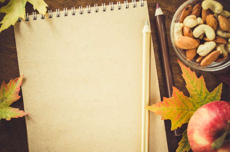 Flat lay of blank brown notebook with nuts, apples and autumn leaves on wooden table. Autumn still life. Cozy autumn mood. Copy space.の写真素材