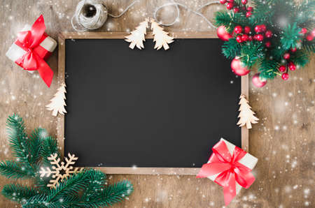 Empty blackboard with christmas decoration, red gift box, fir branches. Chalk board and Christmas trinkets. Xmas background with copy space for inscription, top view. Snow effect.の写真素材