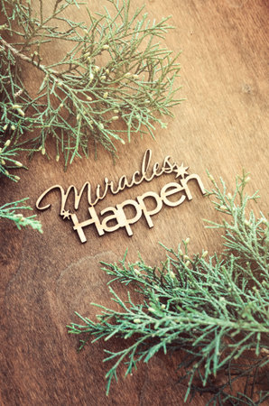 Inscription miracles happen and fir branches on a wooden background. Concept of inspiration and...